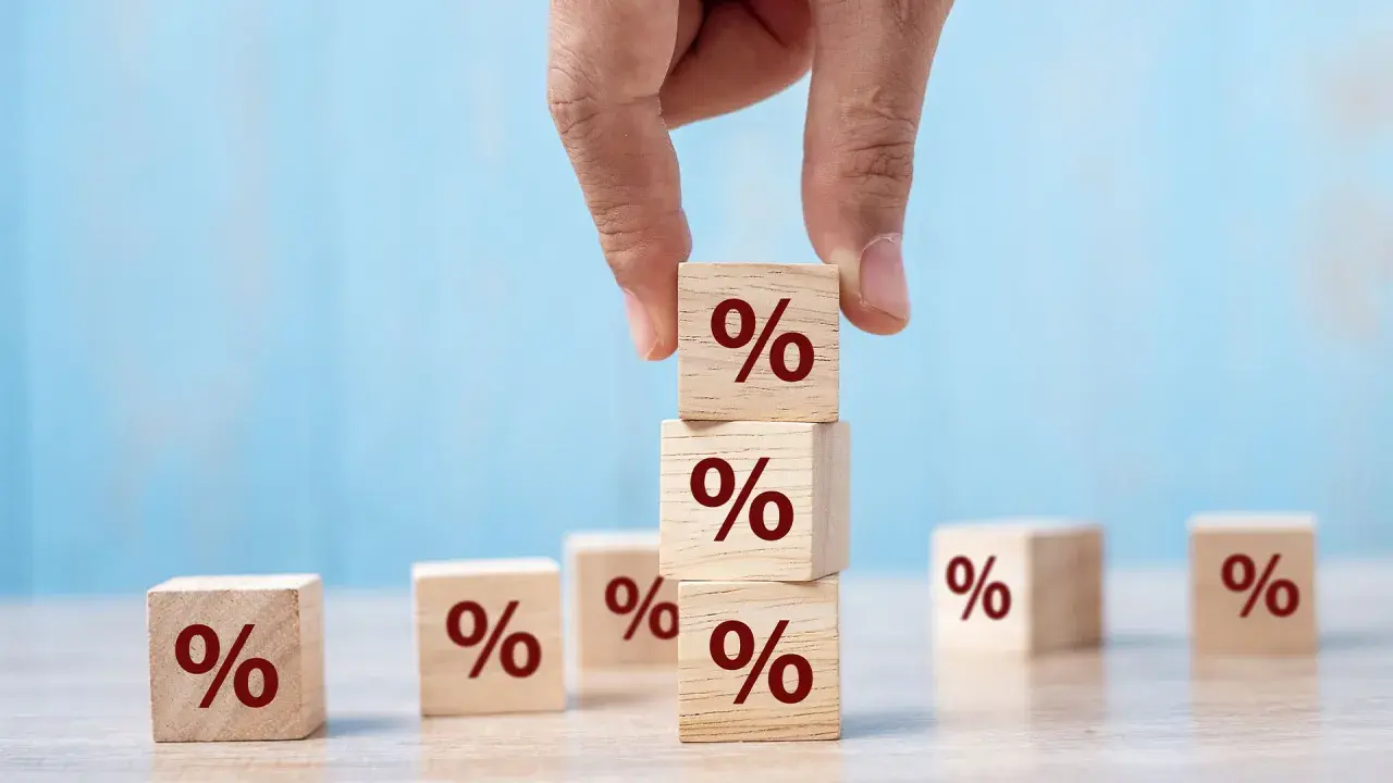 Main d'une personne empilant des cubes en bois marqués du symbole "%", symbolisant le calcul du taux de remplacement retraite.