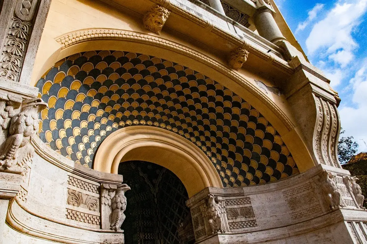 Dettaglio architettonico con decorazioni a squame dorate e blu, sculture di aquile e teste leonine. Un esempio di architettura del quartiere Coppedè.
