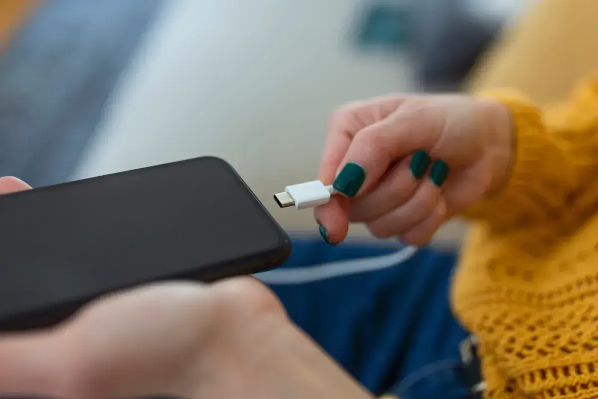 Dłoń z zielonymi paznokciami próbuje podłączyć kabel do telefonu, ale telefon się nie ładuje.