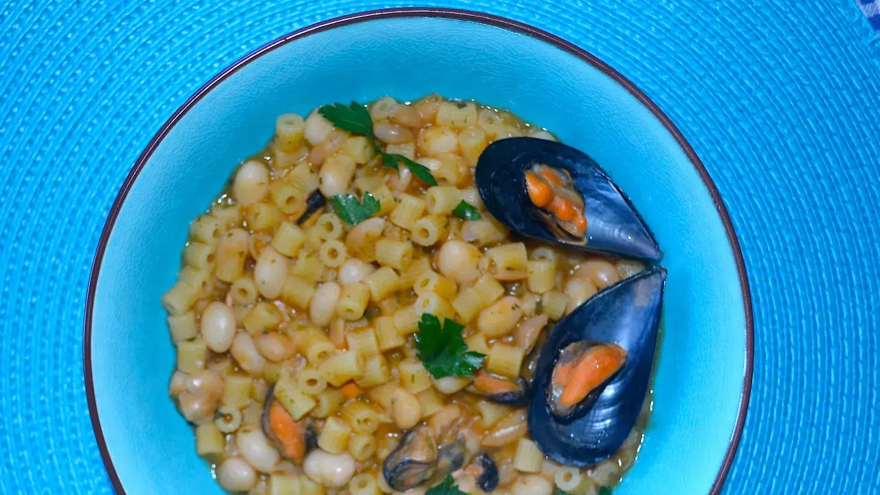 Piatto di pasta fagioli e cozze, un classico della cucina italiana, servito in una ciotola azzurra su un tovagliolo blu.
