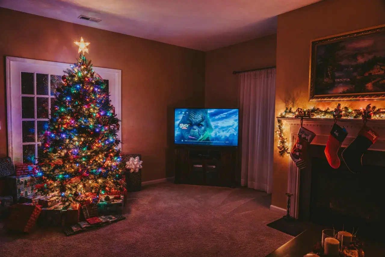 Albero di Natale illuminato, regali sotto, e il Grinch in TV. Perfetto per ascoltare canzoni di Natale in inglese testo.