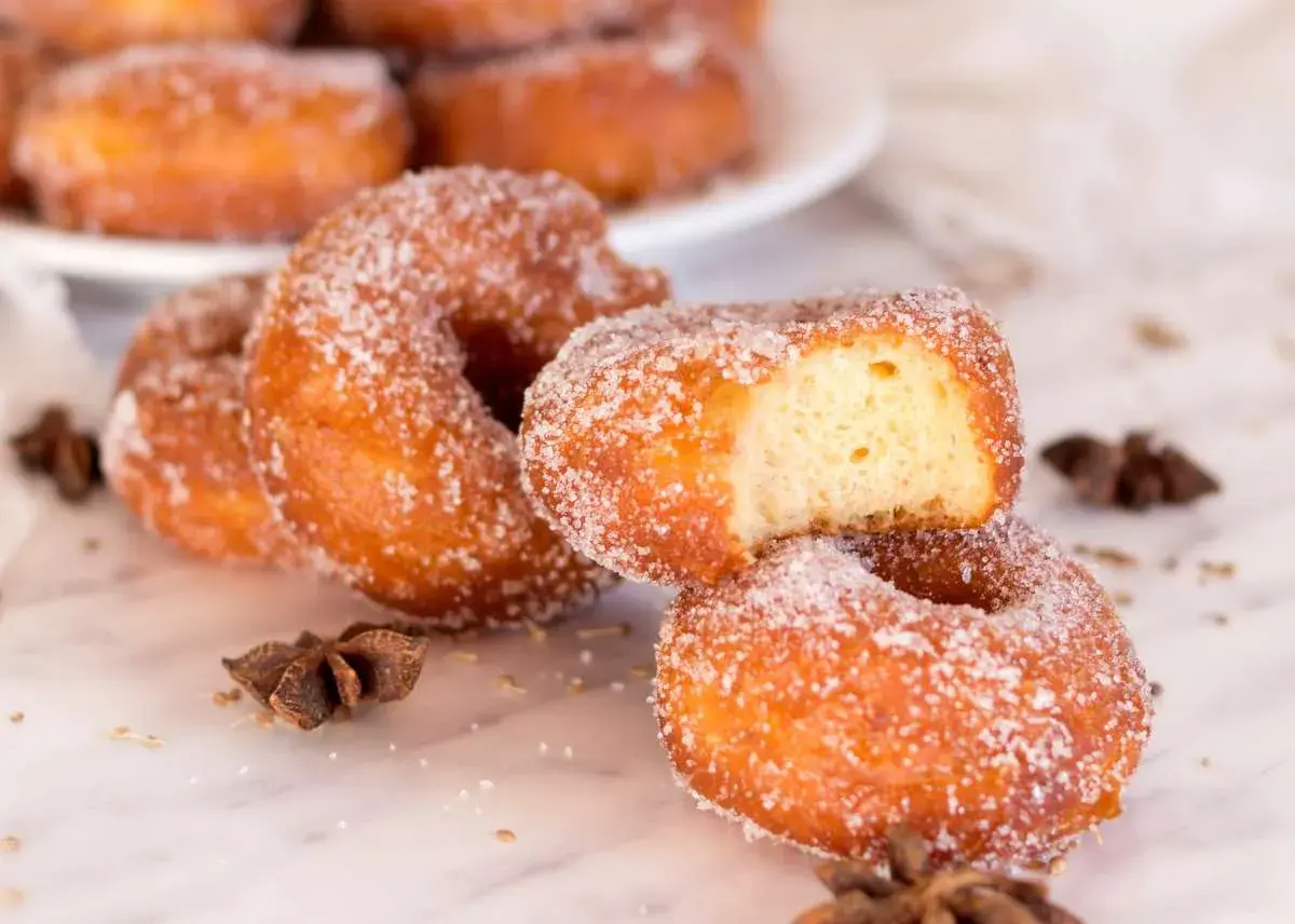 Rosquillas de carnaval espolvoreadas con azúcar, una con un mordisco, junto a anís estrellado.