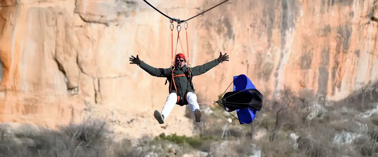 Hombre disfrutando de una tirolina de cuenca, con los brazos extendidos y una gran sonrisa, mientras desciende por un acantilado.