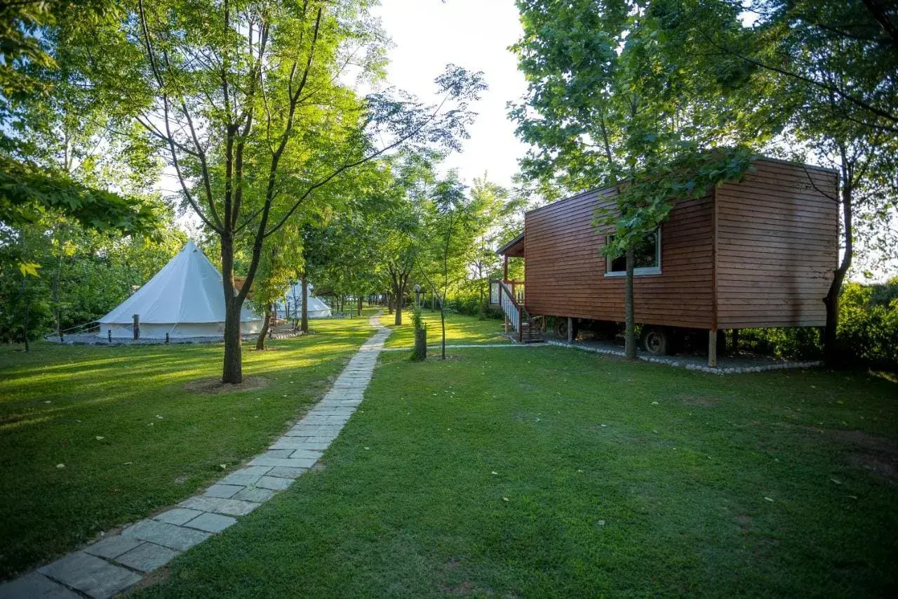 Glamping w Albanii, blisko morza jońskiego. Białe namioty i drewniany domek na wzgórzu, otoczone zielenią.