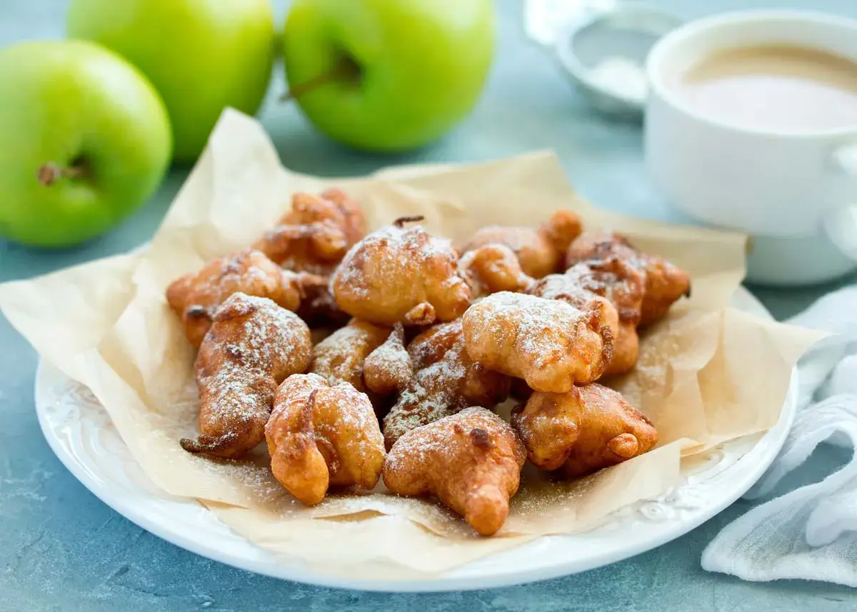 Montón de buñuelos de manzana dorados y espolvoreados con azúcar glas, listos para disfrutar.