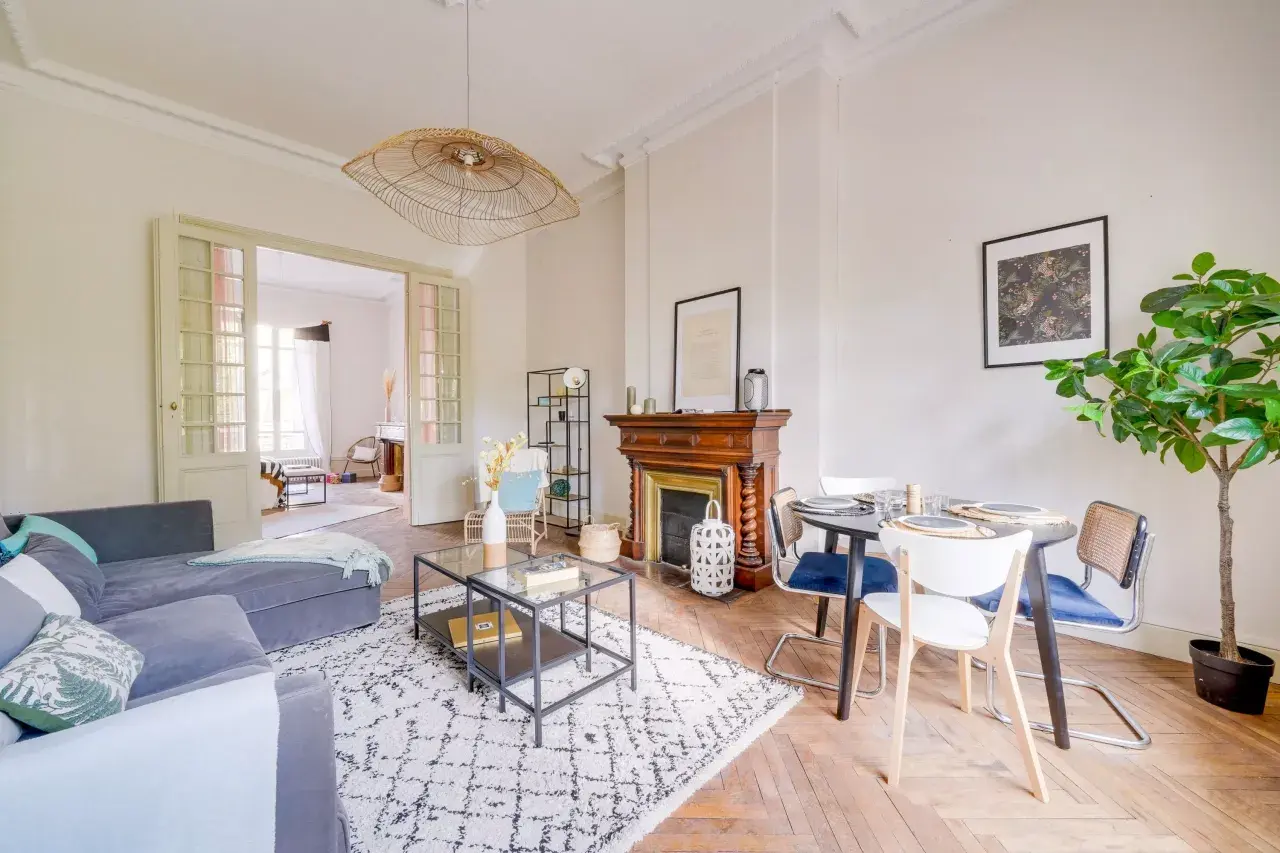 Salon lumineux avec canapé gris, tapis graphique, cheminée ancienne et table à manger. Une belle idée home staging pour un espace convivial.