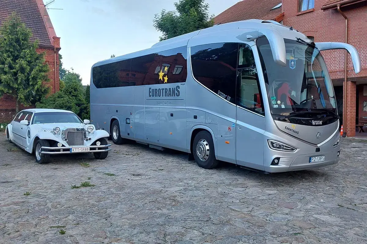 Biała limuzyna i szary autokar stoją obok siebie na brukowanym dziedzińcu.