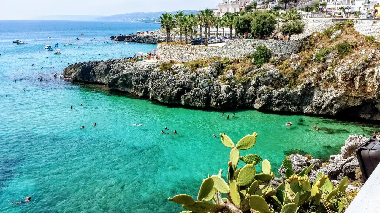 Scogliera con mare cristallino e gente che nuota, tipica dei paesi sul mare in Puglia.