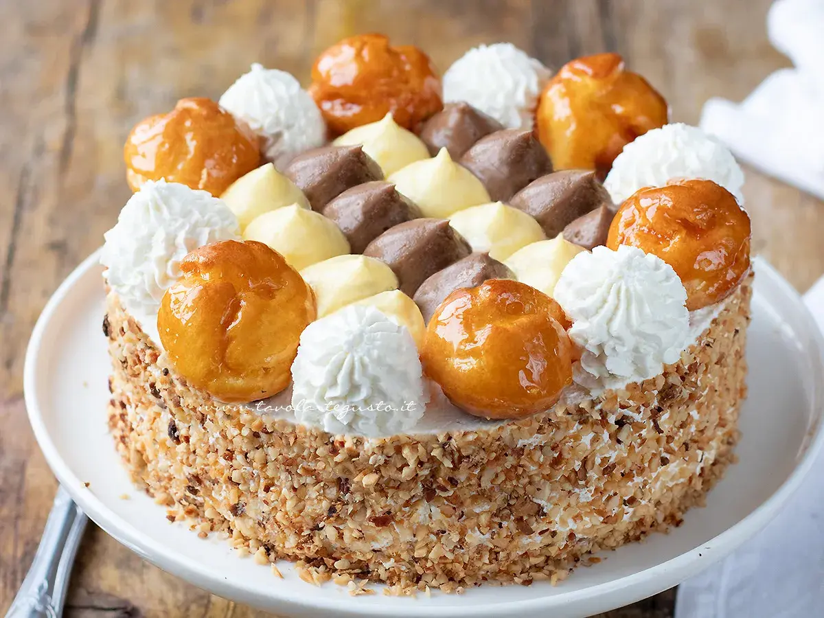 Una magnifica torta Saint Honoré, decorata con bignè caramellati, ciuffi di panna montata e crema pasticcera al cioccolato e vaniglia.