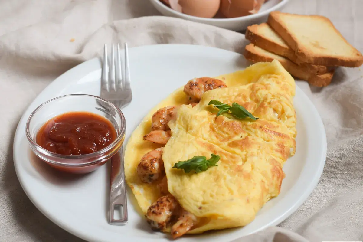 Tortilla de gambas dorada y jugosa, servida con salsa y tostadas. Un desayuno perfecto.