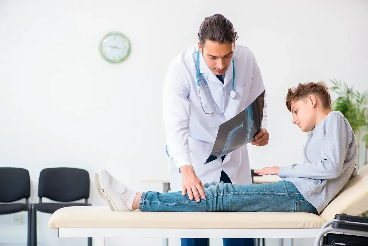 Arzt erklärt Röntgenbild einem Jungen, der auf einer Liege sitzt. Möglicherweise geht es um Orthese Druckstellen.