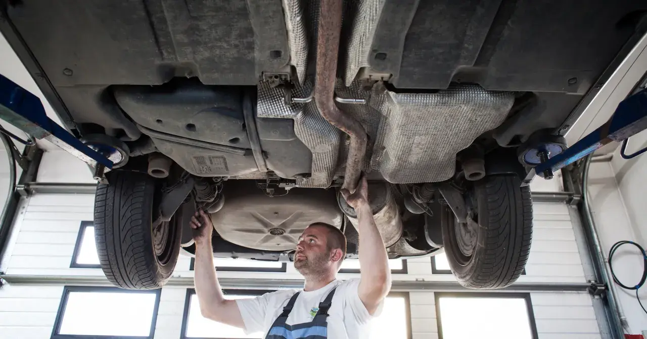 Mechanik sprawdza podwozie sedana na podnośniku, badając układ wydechowy i zawieszenie.