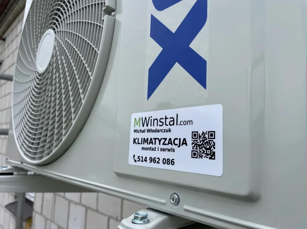Zewnętrzna jednostka klimatyzacyjna z naklejką firmy MWinstal.com.