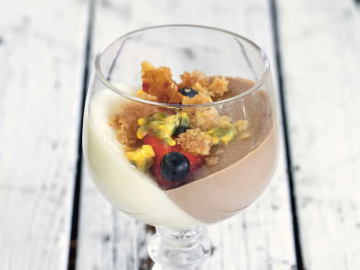 En läcker pannacotta med vit choklad, toppad med bär och smulor.