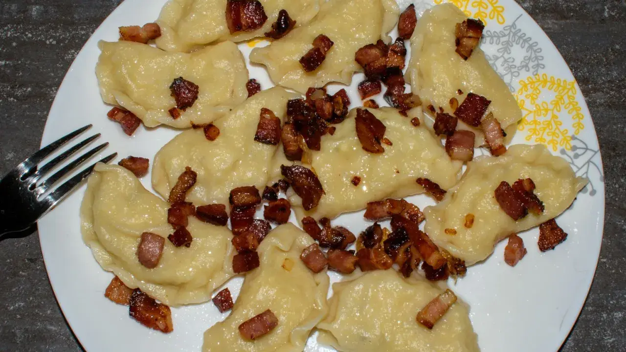 Pyszne pierogi galicyjskie z chrupiącym boczkiem na talerzu. Obok leży widelec.