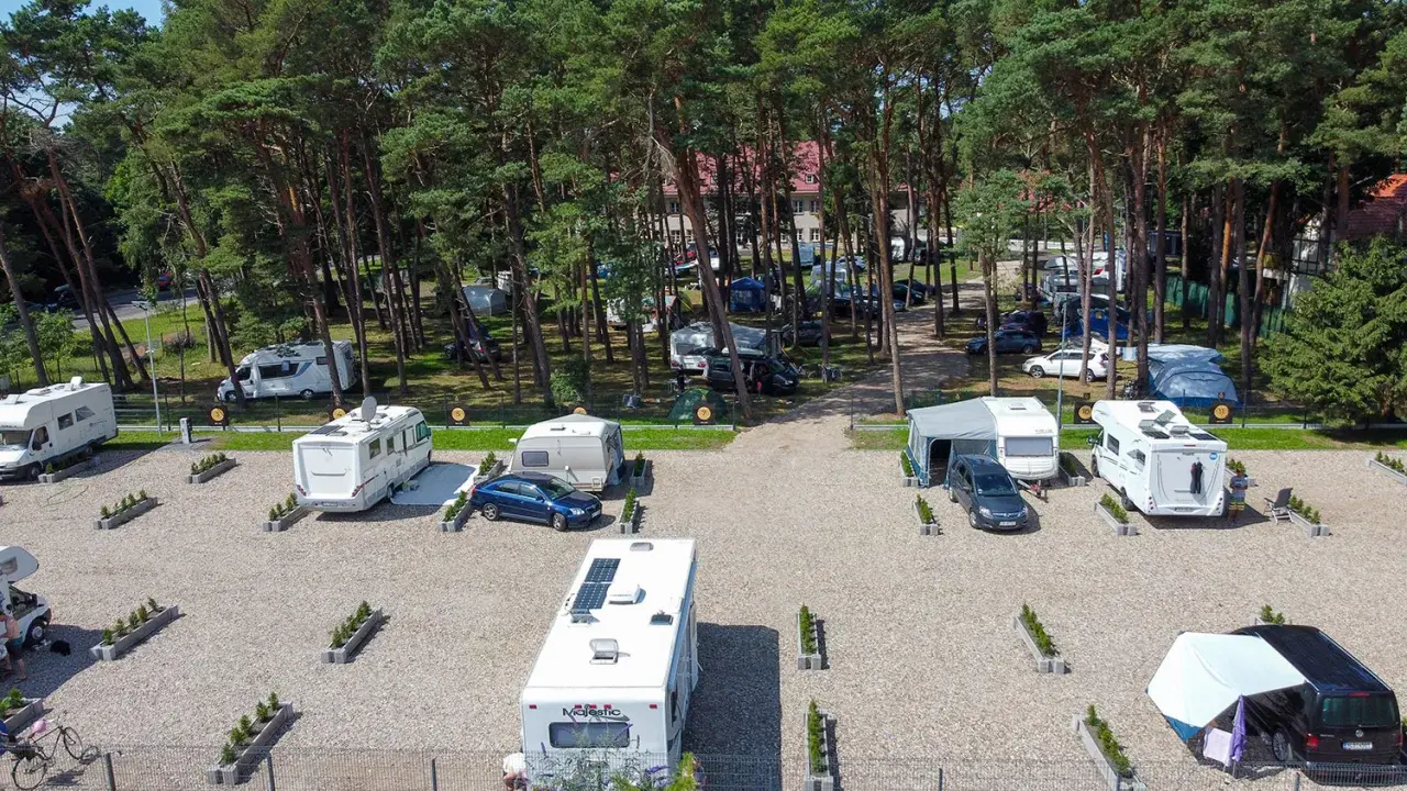 Kampery i przyczepy kempingowe na żwirowym polu namiotowym w lesie sosnowym. Widok z lotu ptaka na sea camp Rogowo.