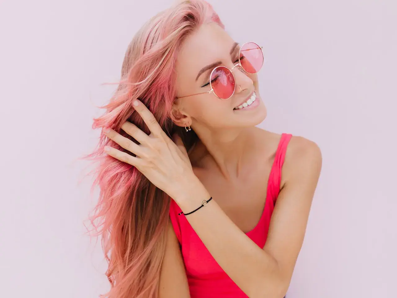 Ragazza con capelli rosa sfumati, occhiali da sole rotondi e un top fucsia. Il suo shampoo colorante mantiene vibrante la chioma.
