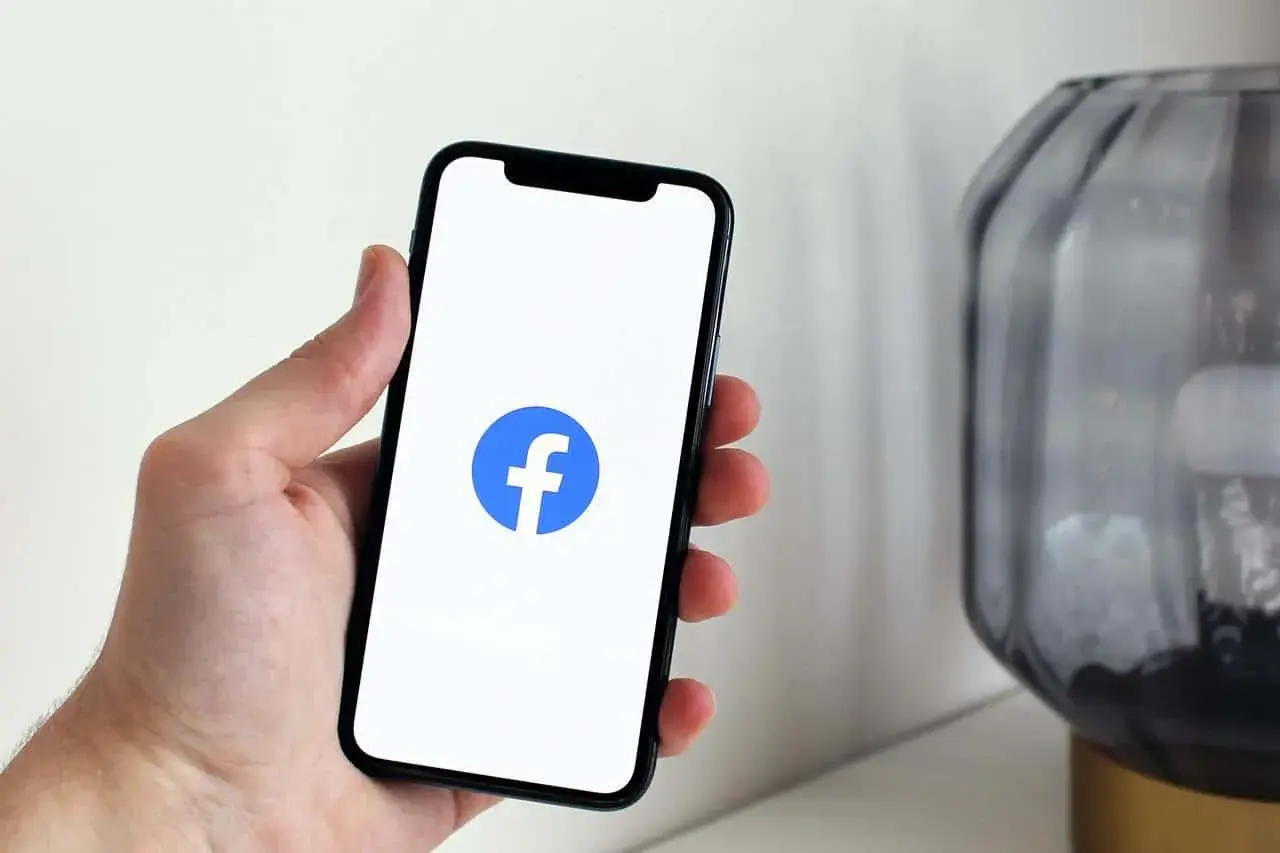 Dłoń trzyma smartfon z logo Facebooka. Dowiedz się, jak dodać zdjęcie profilowe na FB z galerii.