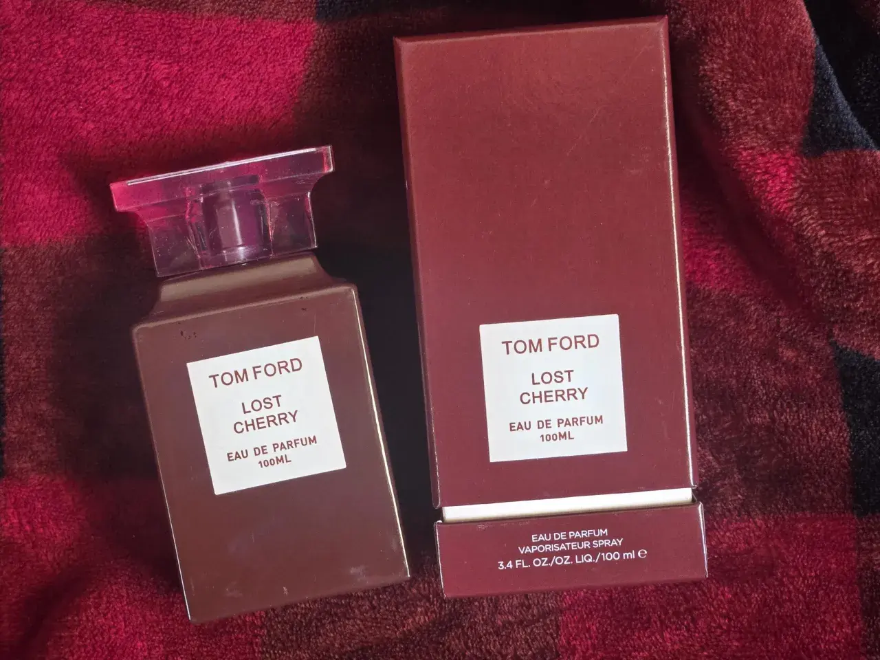 Elegancki flakon i pudełko perfum Tom Ford Lost Cherry 100 ml na tle czerwonego, miękkiego materiału.