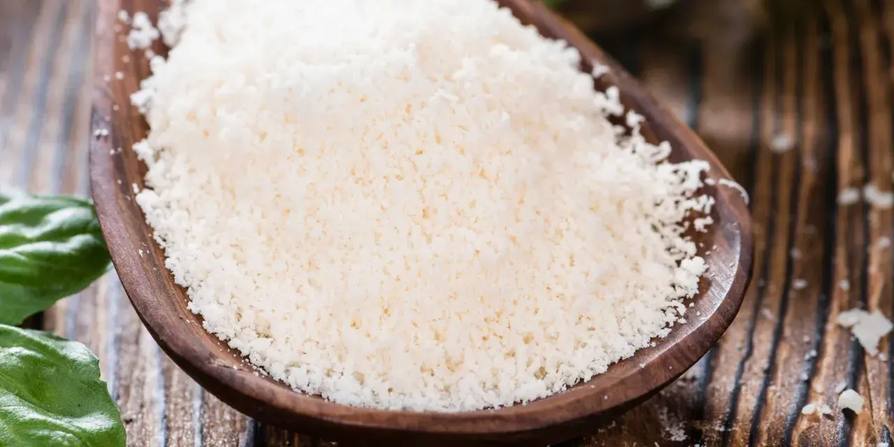Cuchara de madera con rallado fino de parmesano vegano, listo para espolvorear sobre tu plato favorito.