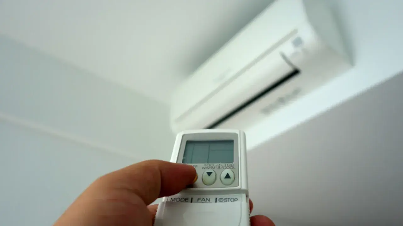 Mano sujetando un control remoto de aire acondicionado, ajustando la temperatura para controlar cuanto gasta un aire acondicionado.