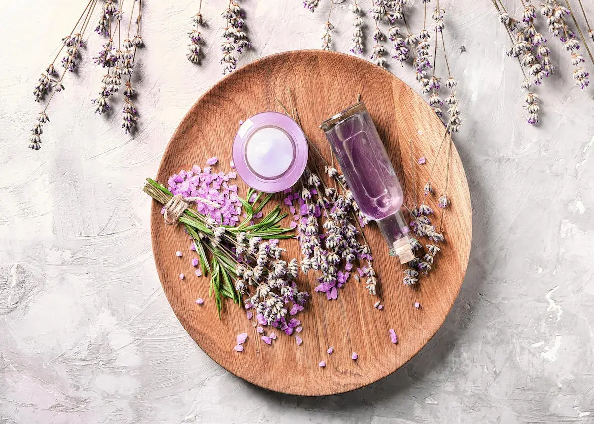 Sur un plateau en bois, des brins de lavande fraîche et séchée, des cristaux violets et une petite bouteille de liquide pour faire bouillir de la lavande.