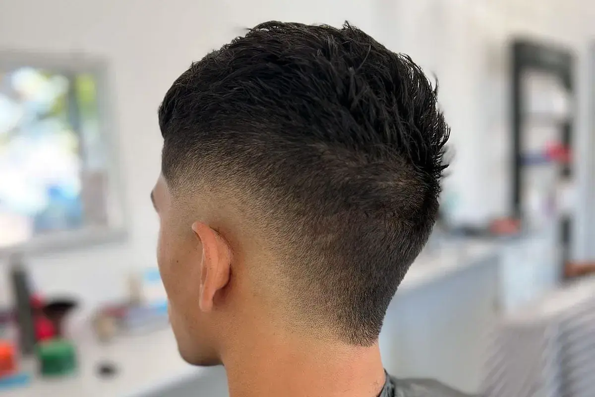 Corte de pelo moderno con un degradado **burst fade** que se desvanece suavemente desde la nuca hacia las orejas.