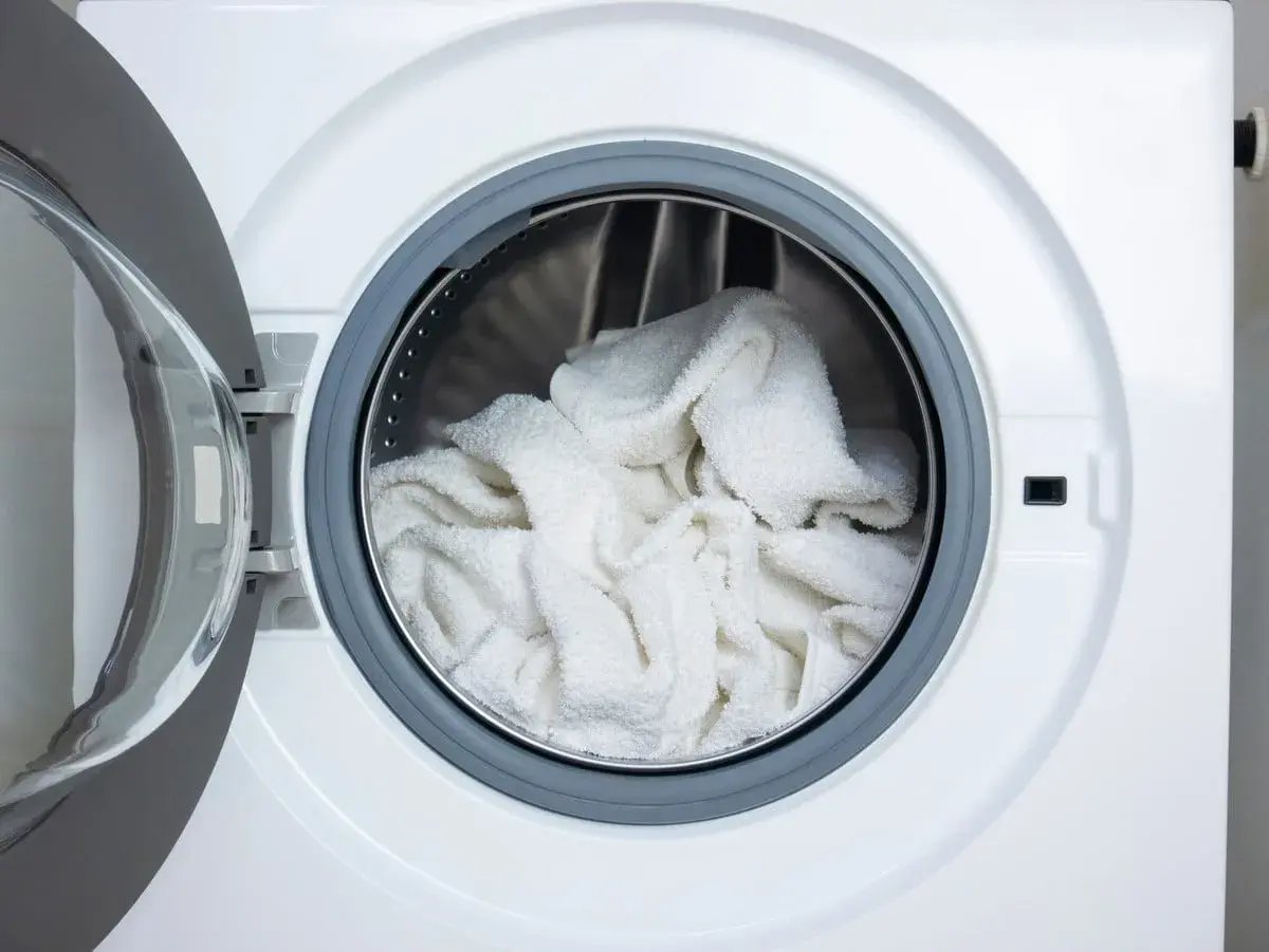 Tambour de machine à laver rempli de linge blanc prêt pour un lavage éclatant avec de l'eau de javel pour blanchir le linge en machine.
