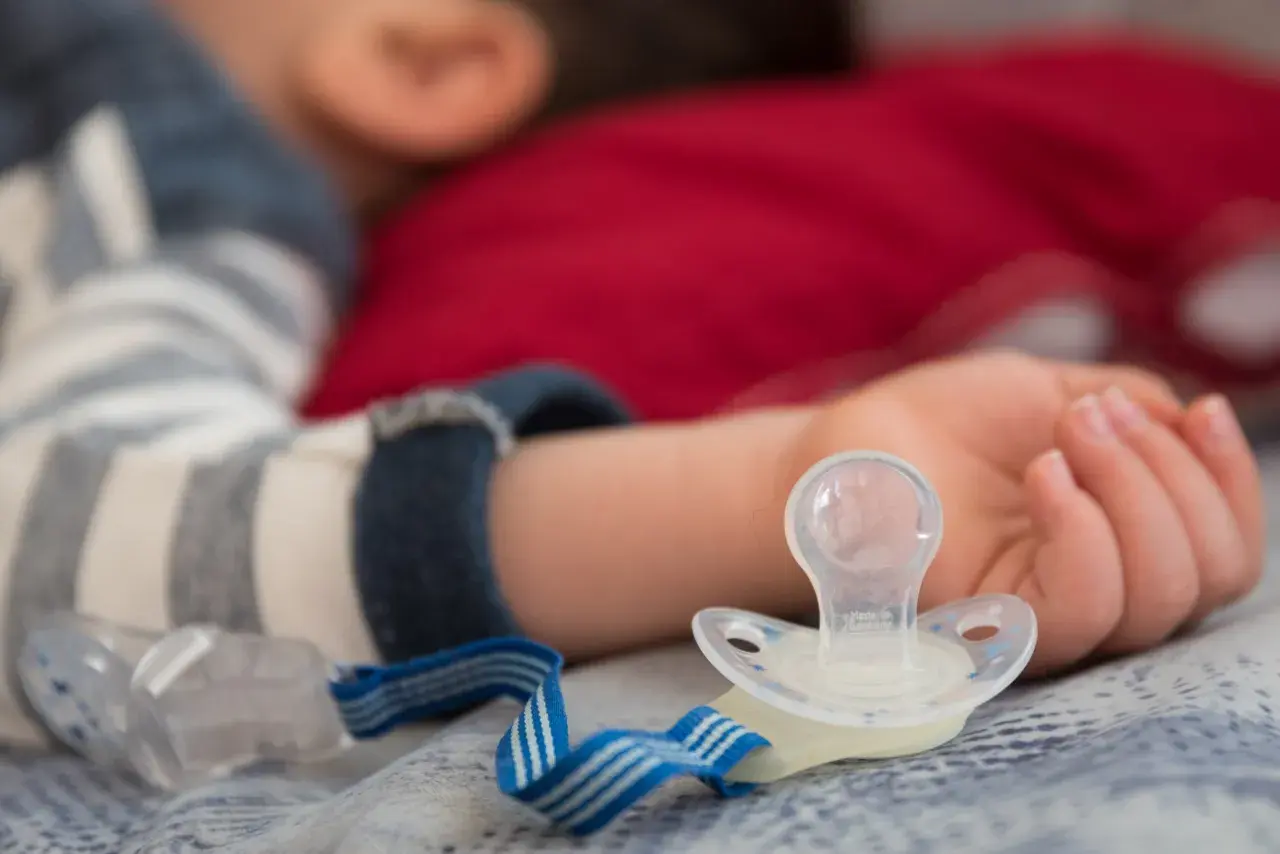 Dziecko śpi z rączką obok smoczka, który może powodować odparzenia.