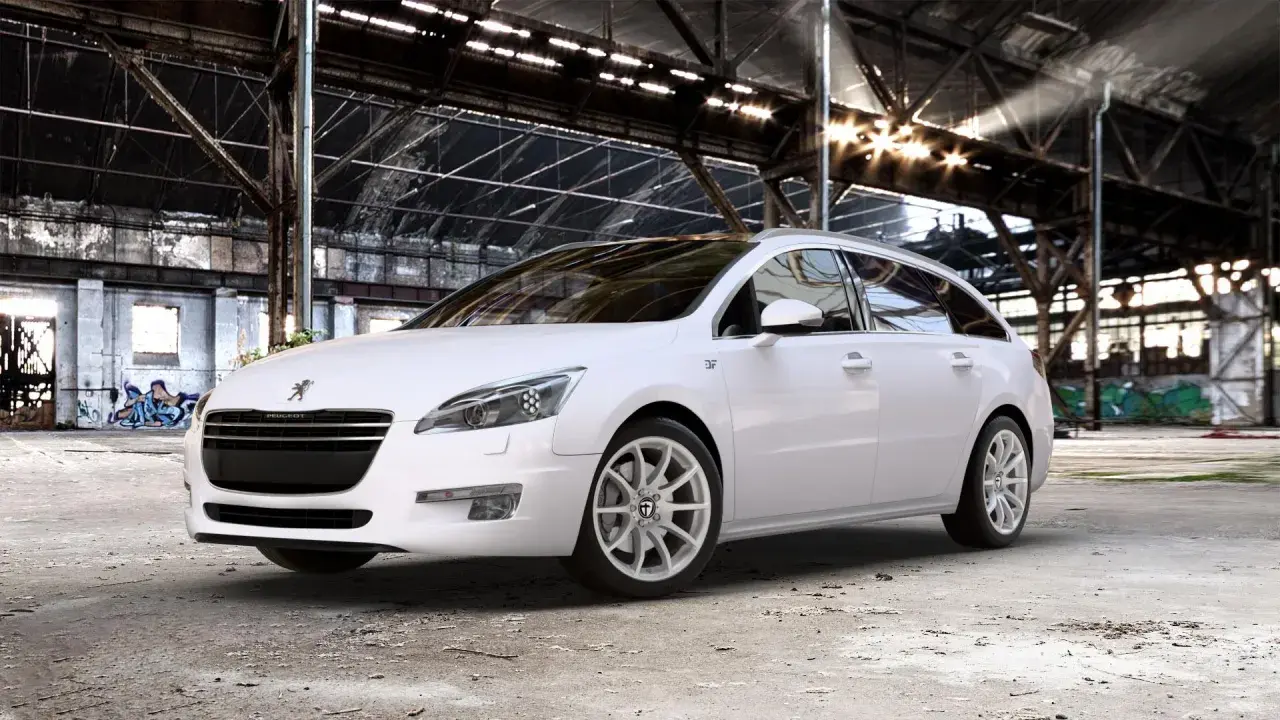 Biały Peugeot 508 SW na jasnych felgach, z widocznym rozmiarem opon, stoi w opuszczonej hali przemysłowej.