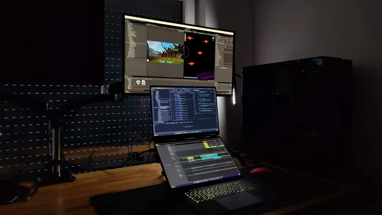 Stanowisko programisty z trzema monitorami, na których widać edytor kodu i scenę gry. Czy c.