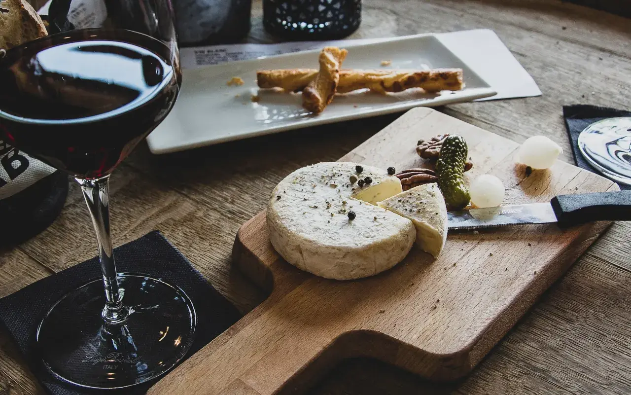 Verre de vin rouge avec un plateau de fromage, cornichons et noix. Un délice pour accompagner une dégustation de vin rouge avec charcuterie et fromage.