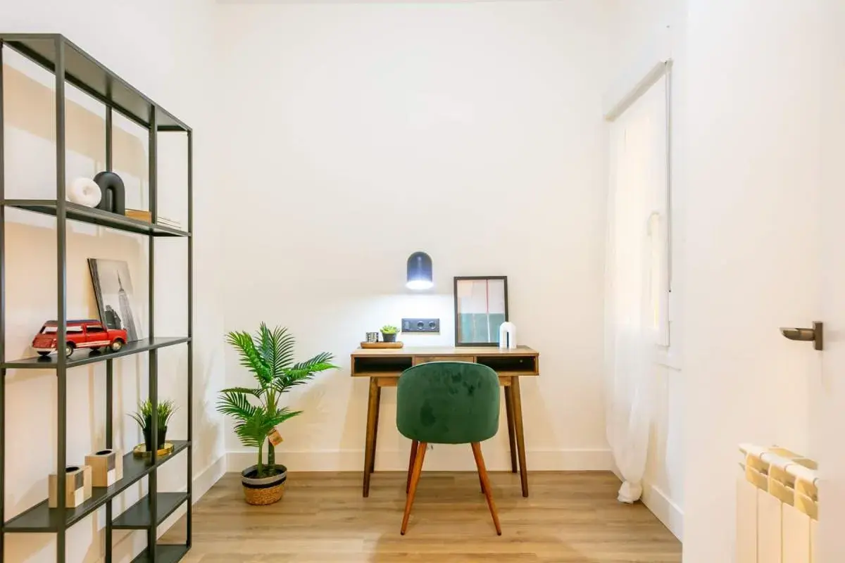 Escritorio de madera con silla verde, planta y estantería metálica. La luz de la lámpara es de 4000 K, creando un ambiente acogedor.