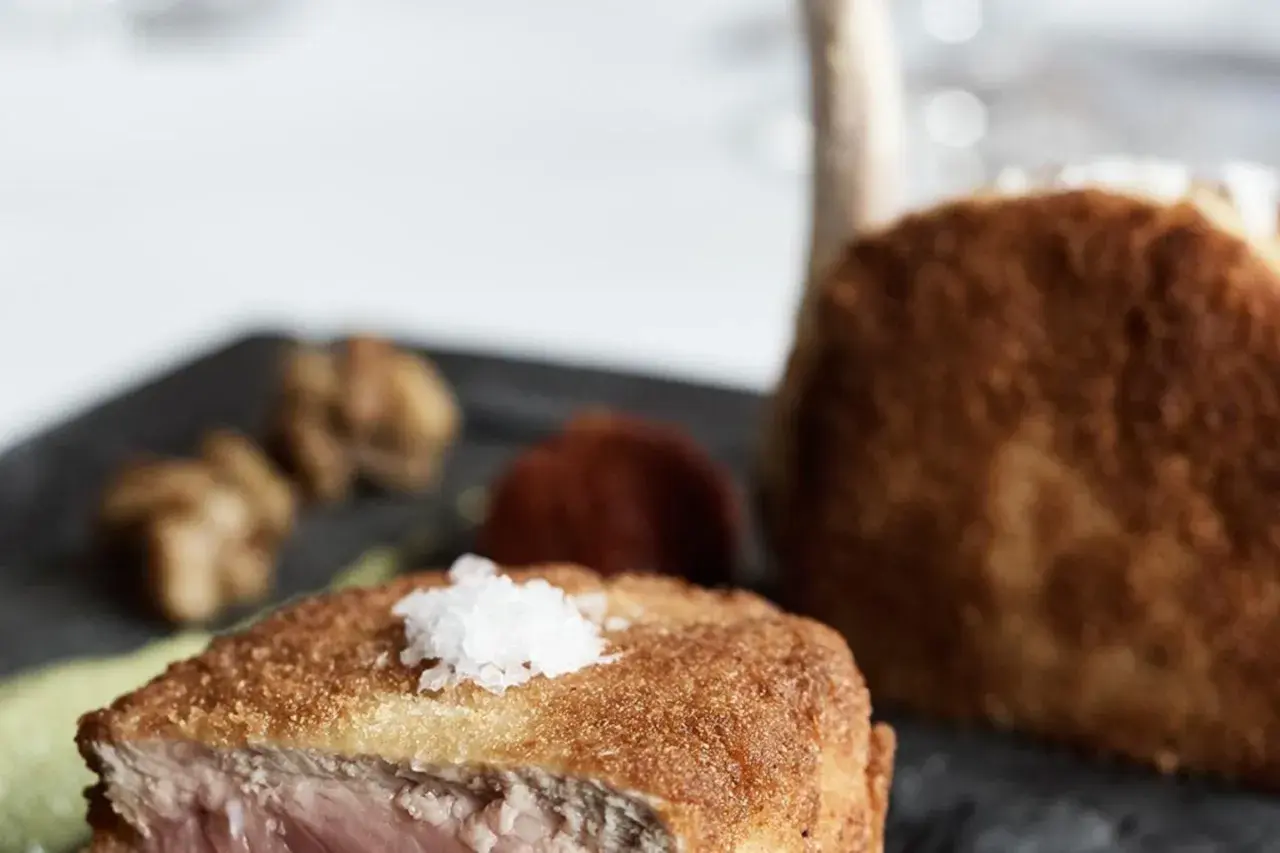 Ein knuspriges Kalbsschnitzel, italienisch zubereitet, mit feinen Beilagen auf einem dunklen Teller.