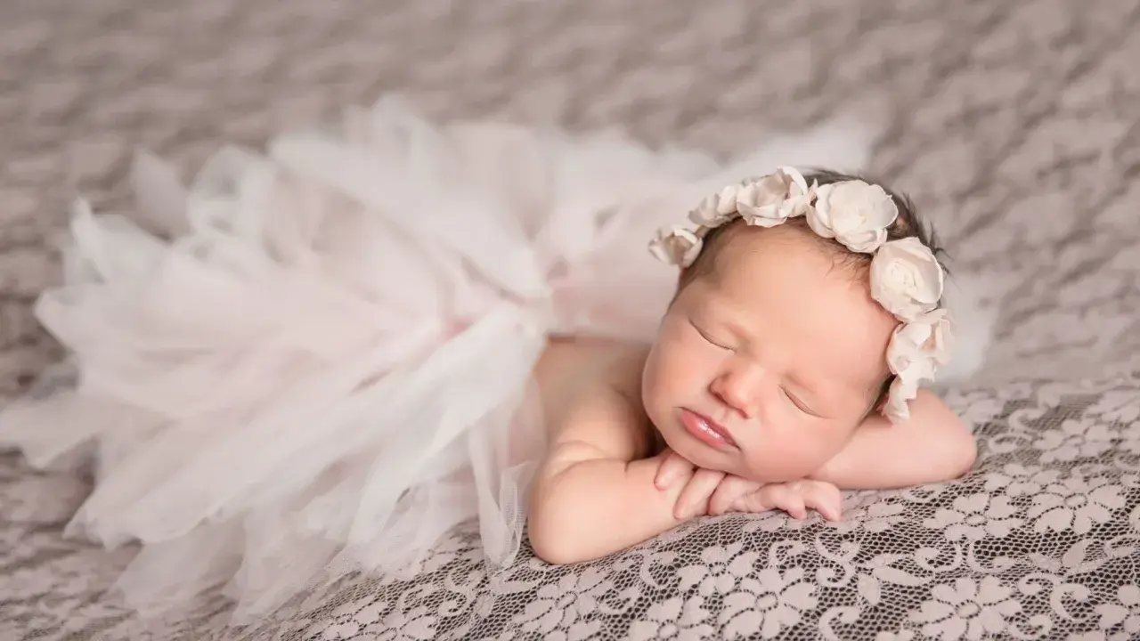 Un bébé endormi, paré d'une couronne de fleurs et d'une jupe en tulle, évoque la douceur et la pureté. Sa pose paisible invite à réfléchir à la signification prénom.