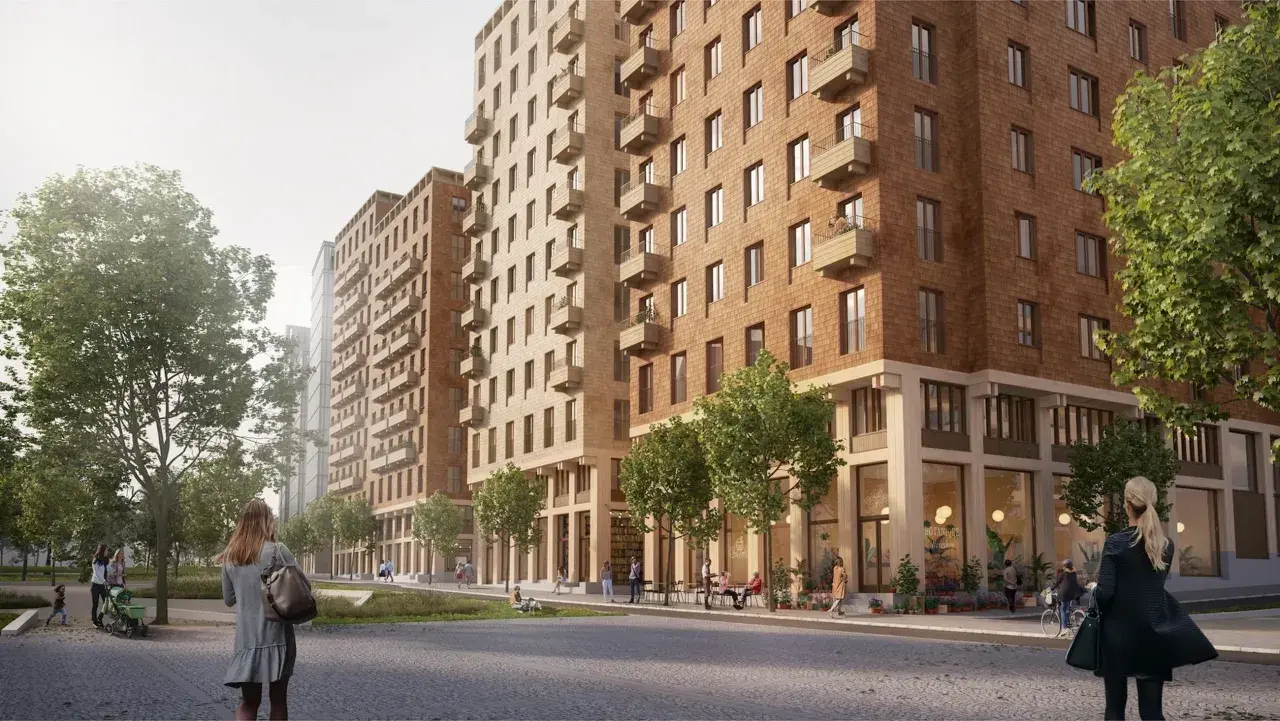 En modern stadsbild i Sverige med tegelbyggnader, balkonger och grönska. En kvinna med en väska går längs en stenlagd gata.