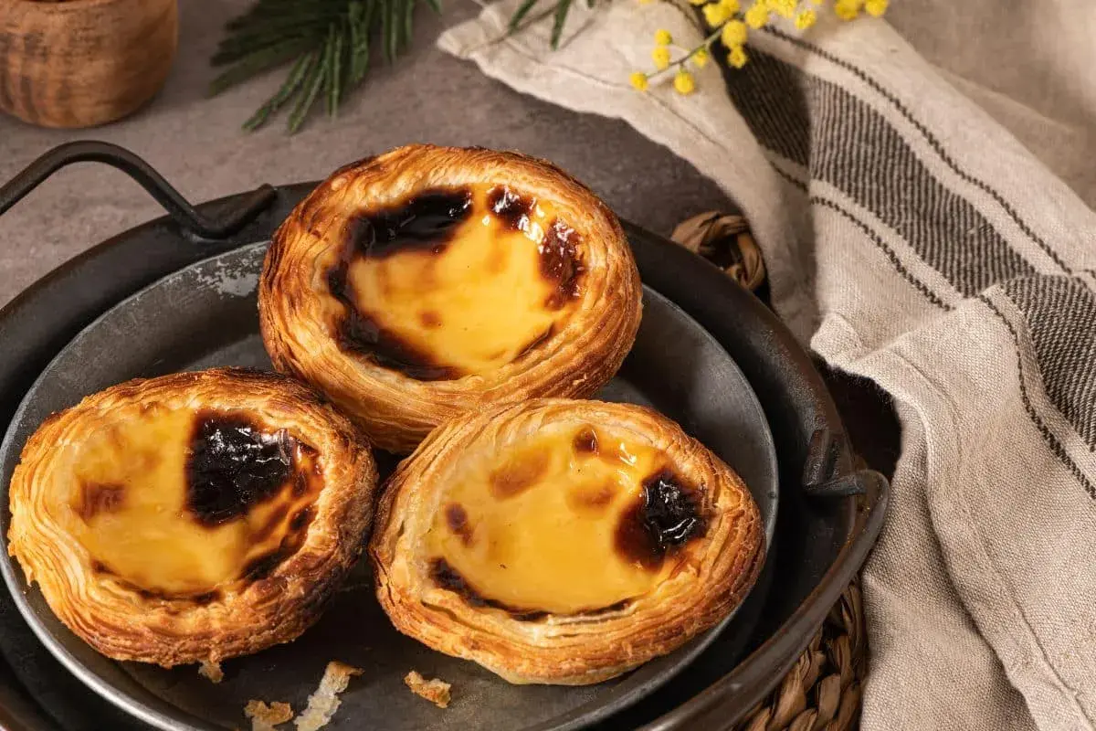 Trois délicieux flans portugais, dorés et caramélisés, sur un plateau en métal.