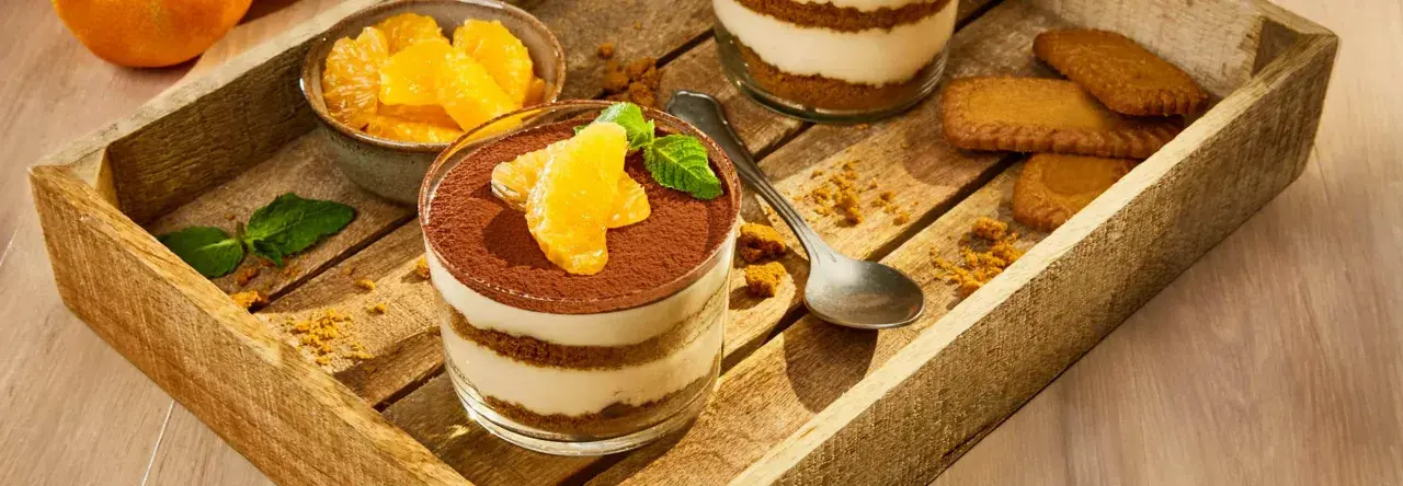 Délicieux tiramisu aux fruits d'orange, garni de cacao et de menthe fraîche, servi dans un verre sur un plateau en bois avec des biscuits.