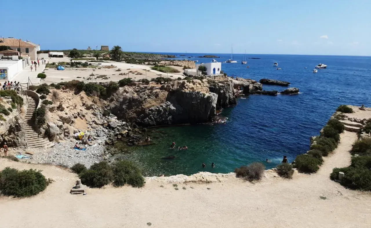 Gente nadando y tomando el sol en las calas de la isla Tabarca, con aguas cristalinas y barcos en el horizonte.