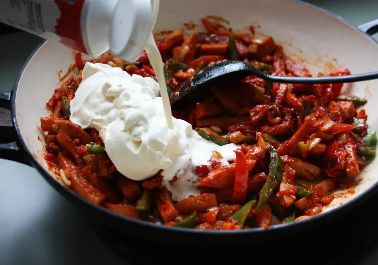 Gräddig korvgryta recept i pannan. Korv, paprika och lök blandas med en stor klick grädde.