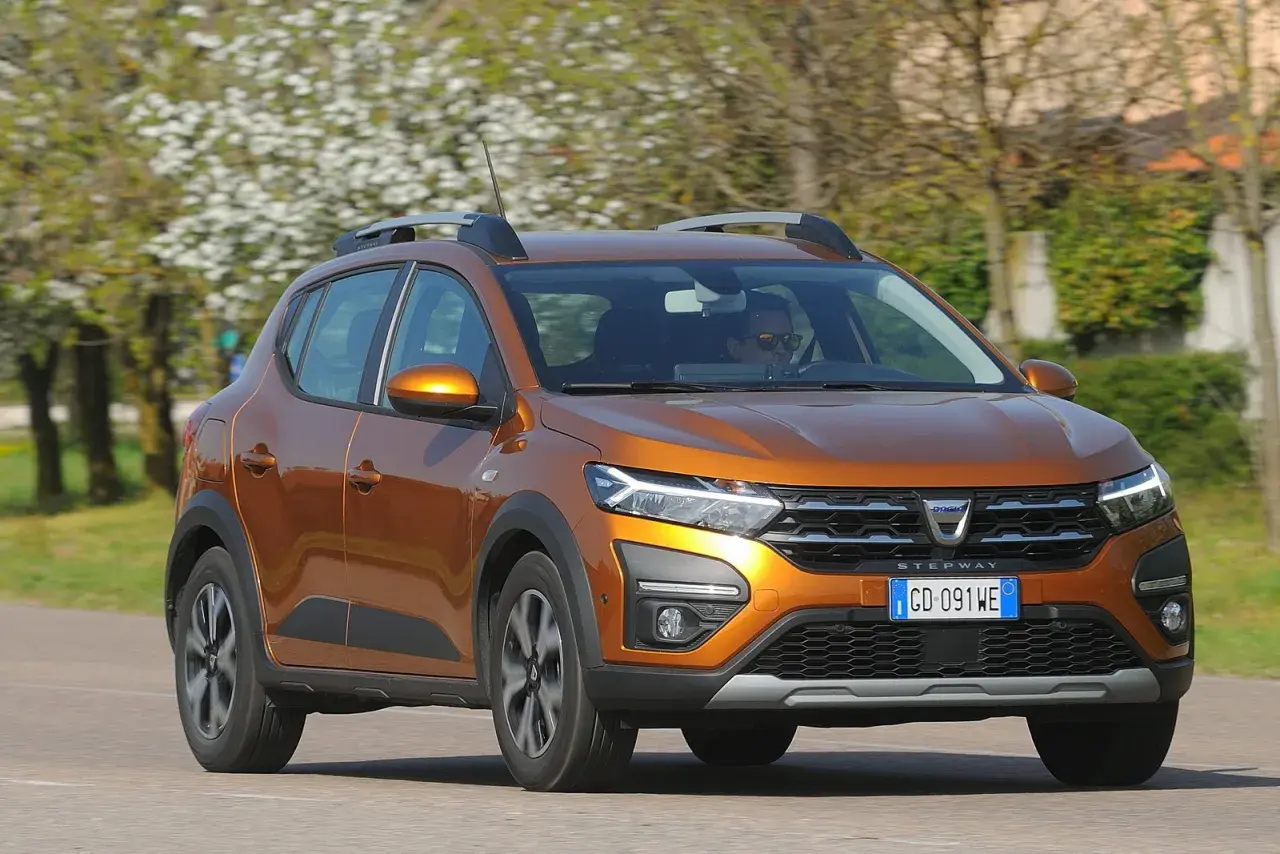 Dacia Sandero Stepway arancione in movimento, con alberi fioriti sullo sfondo. Nonostante i suoi pregi, alcuni difetti Dacia Sandero Stepway sono noti.