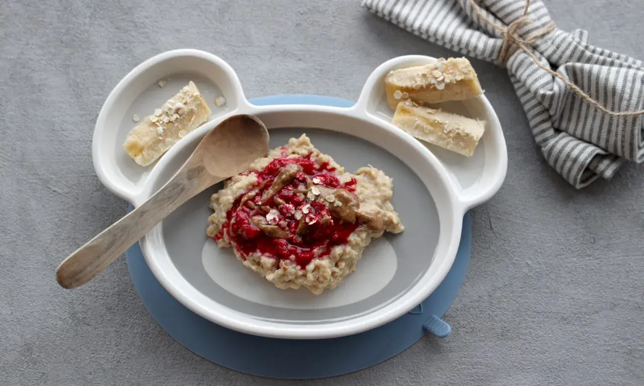 Leckerer Morgenbrei für Babys mit Beeren und Bananenstückchen auf einem Teller in Bärenform.