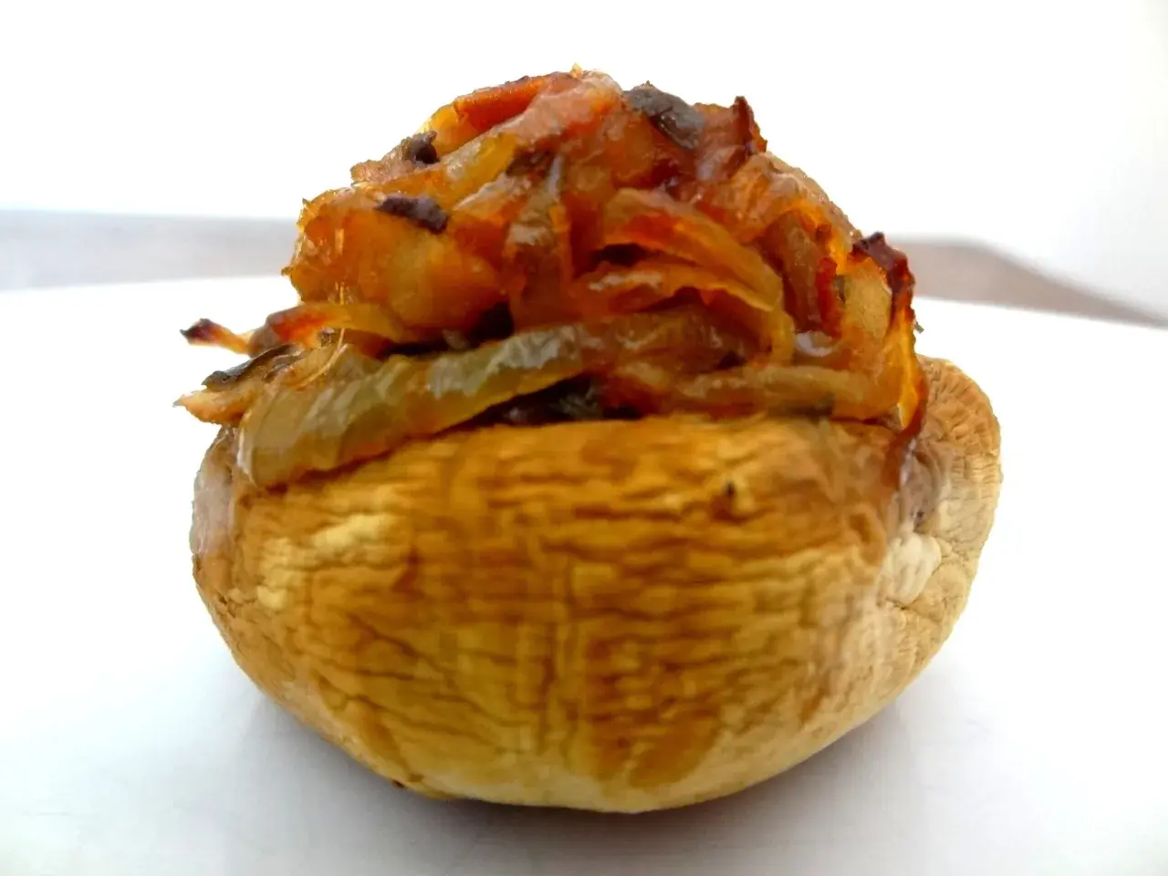 Gros plan sur un champignon farci, garni d'oignons caramélisés et d'herbes. Un délice à savourer !