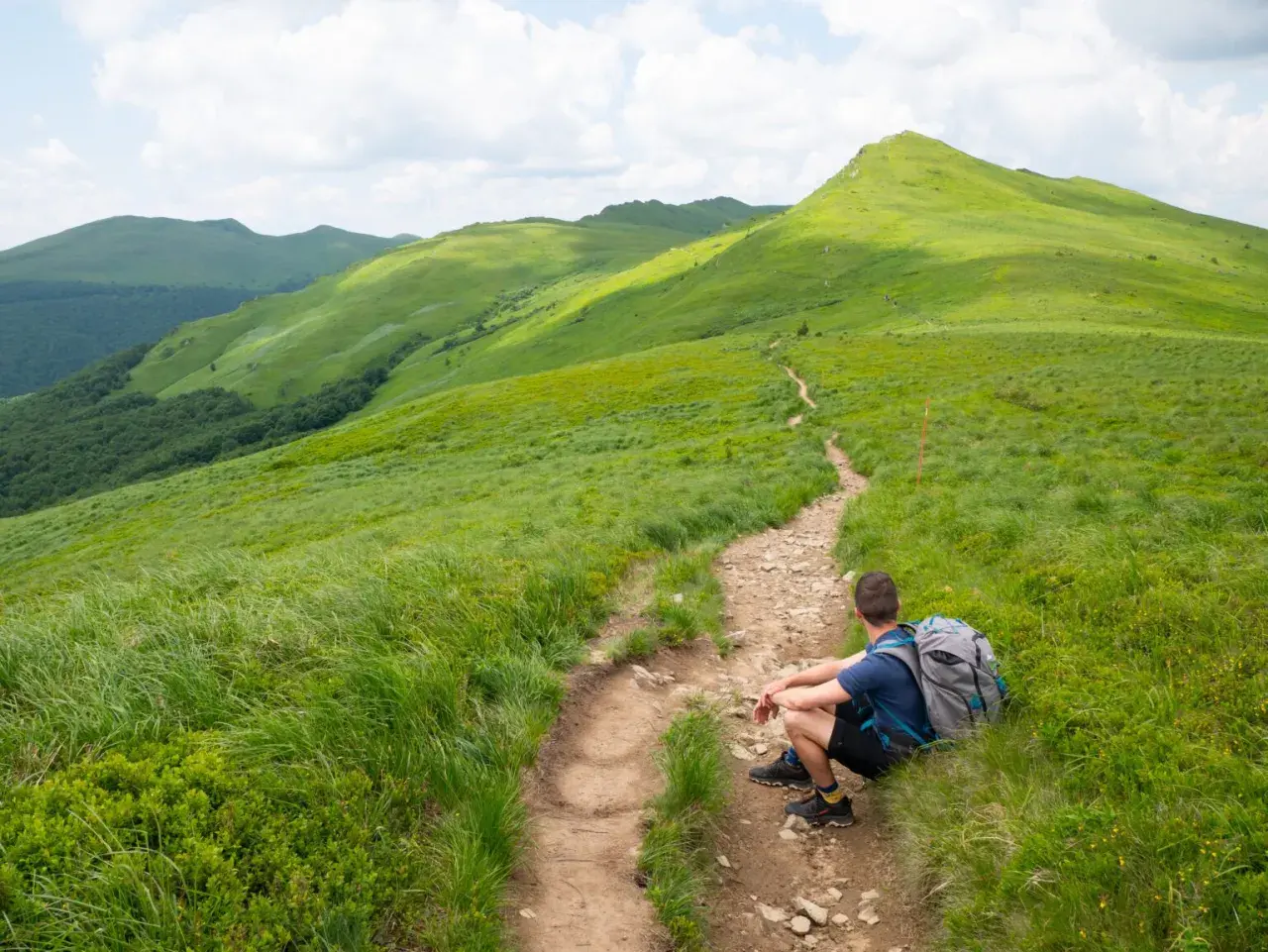 Turysta odpoczywa na szlaku, podziwiając zielone połoniny. Bieszczady atrakcje czekają!