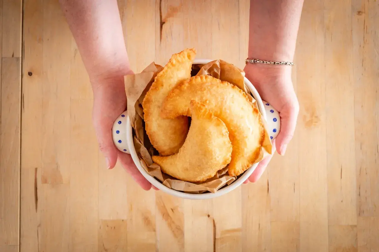 Mani che offrono un cestino di frittelle dorate, un sapore autentico di street food pugliese.