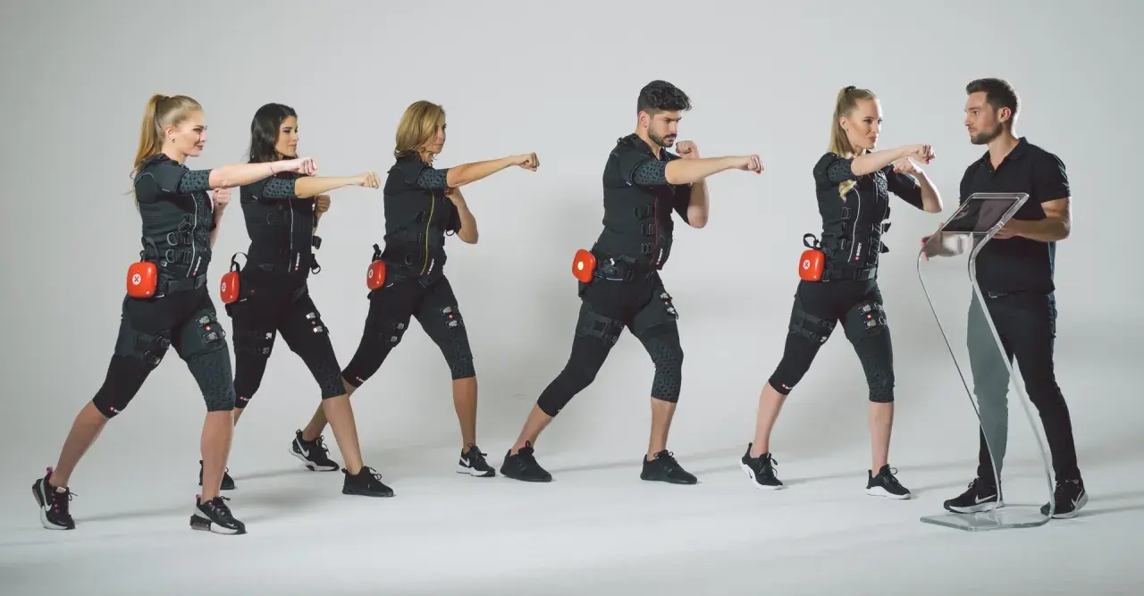 Grupa osób w strojach EMS ćwiczy pod okiem trenera. Dowiedz się, ile kosztuje trening EMS i zacznij swoją metamorfozę!