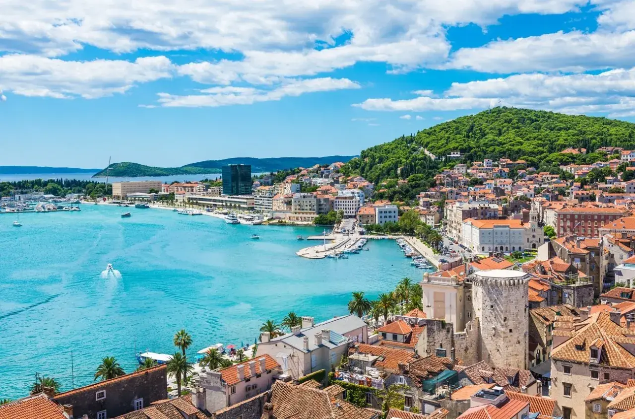 Widok na Split z turkusową wodą, łodziami i zielonym wzgórzem. Ciekawe chorwackie miasto pełne historii.