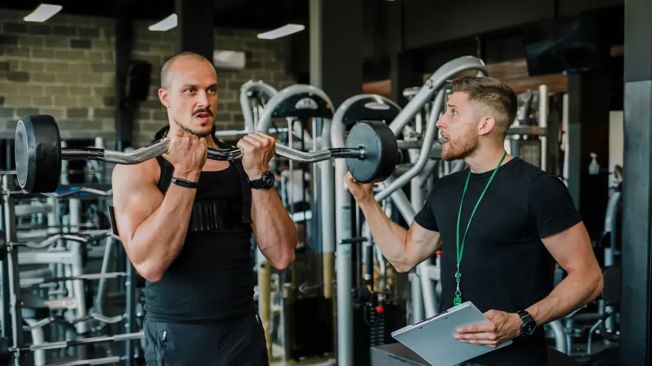 Trener instruuje klienta, jak wykonać ćwiczenie. Czy to superseria? Dowiedz się, co to jest i jak może pomóc w treningu.