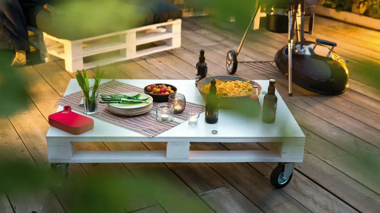 Tavolo fai da te con snack, bevande e candele su un deck di legno, pronto per una grigliata.