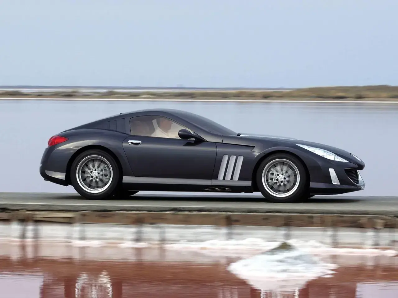 Elegancki, ciemnoszary Peugeot 907 sunie po drodze nad różowym jeziorem.